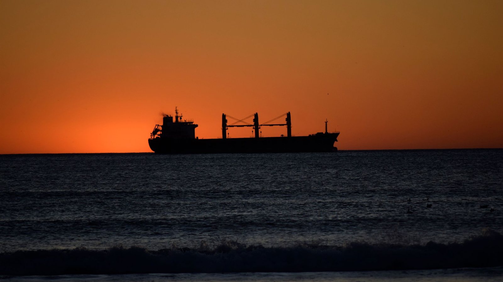 A cargo ship silhouetted against a sunset, representing the physical goods a supplier lifecycle exists to move safely