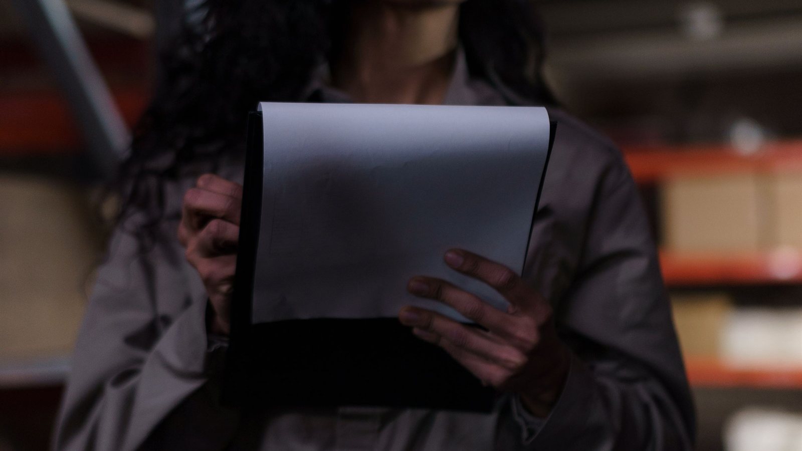 A person holding a clipboard in a warehouse aisle, representing a physical verification visit to a supplier site
